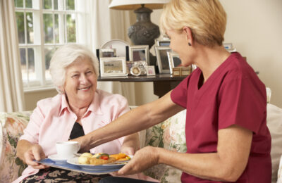 Helper Serving Senior Woman With Meal In Care Home